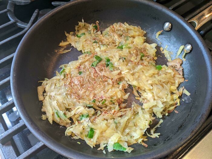 Shredded potatoes and green onions frying in a pan, a simple yet potentially stupid vegan food dish.