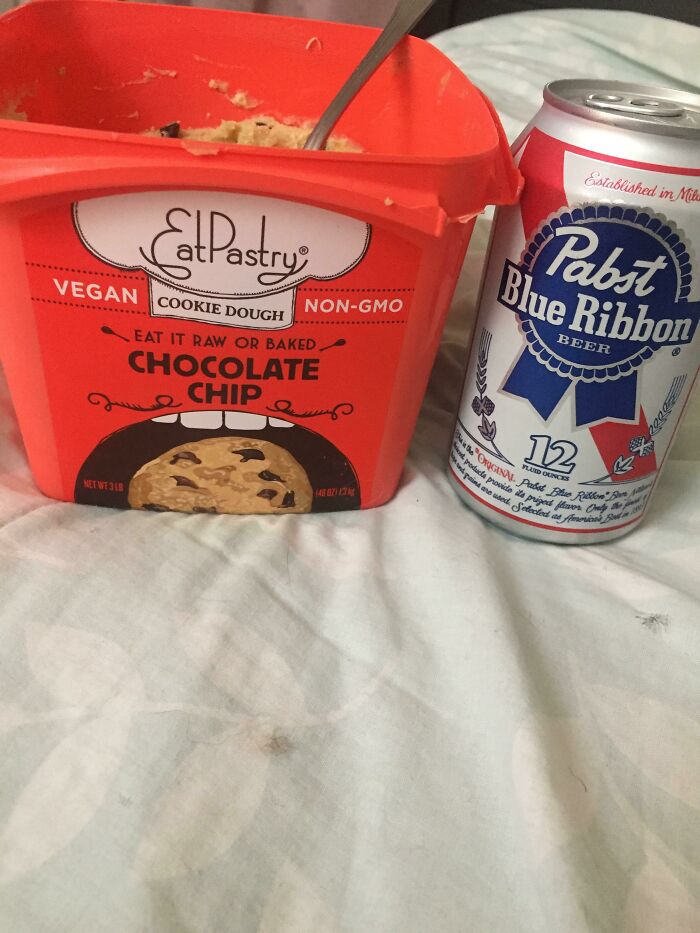Chocolate chip vegan food cookie dough and a can of Pabst Blue Ribbon beer on a bed, showing a stupid vegan food choice.