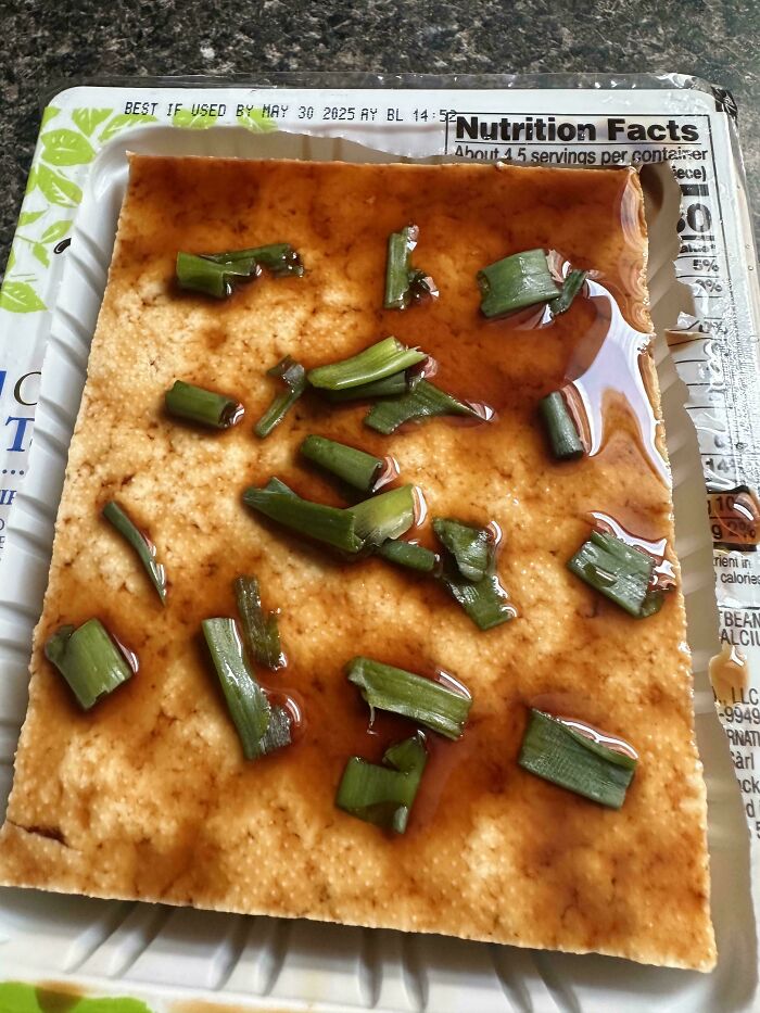 Stupid vegan food: A slab of tofu drizzled with sauce and topped with chopped green onions in its packaging.