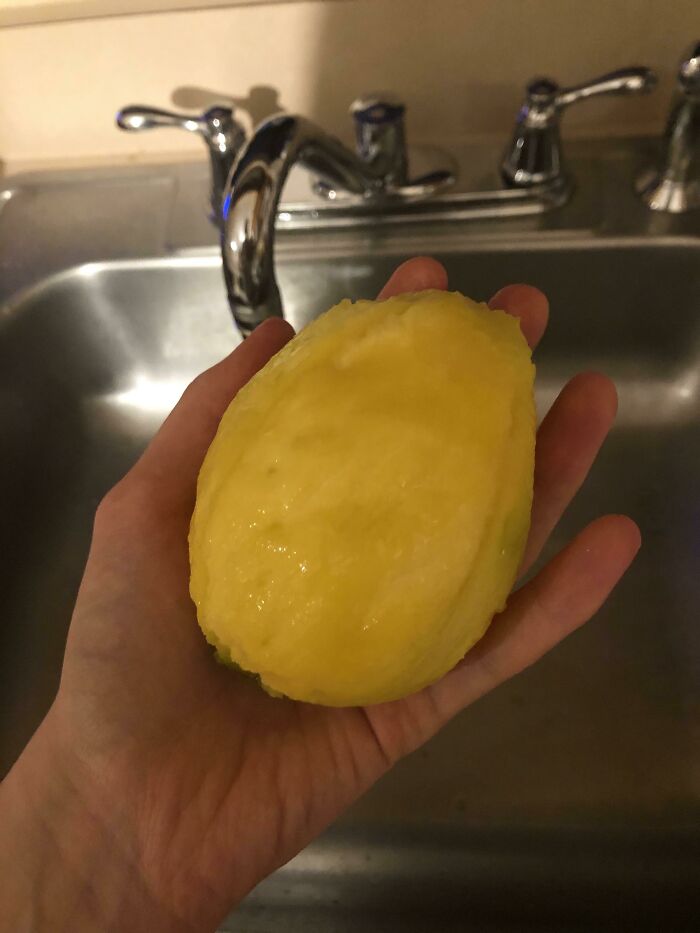 Stupid vegan food: A hand holds a peeled lemon over a stainless steel kitchen sink with faucets.