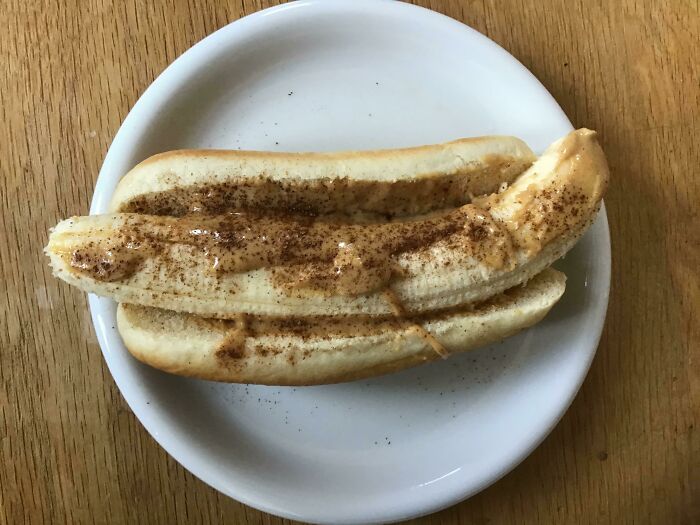 A peeled banana in a hot dog bun, topped with peanut butter and cinnamon, an example of stupid vegan food.