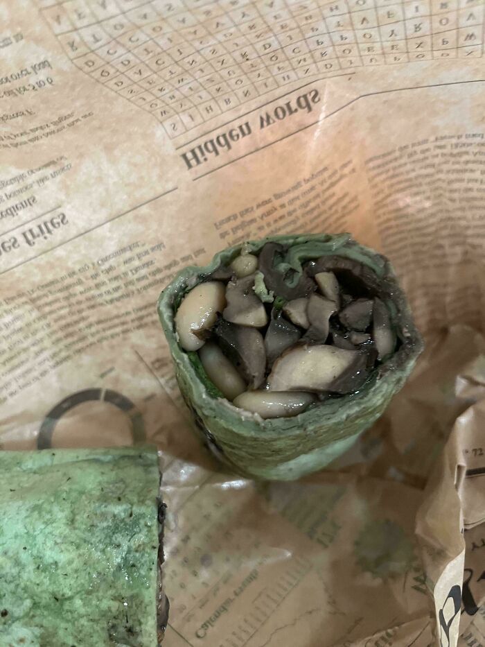 A cross-section of a green wrap filled with mushrooms and white beans, wrapped in paper, representing stupid vegan food.