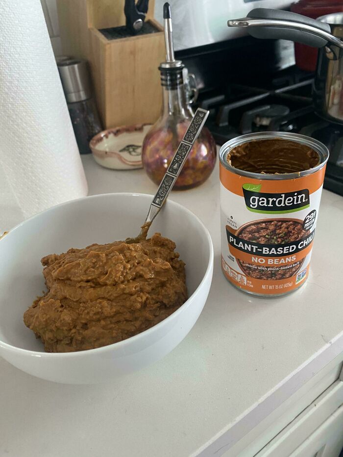 A white bowl filled with plant-based chili next to an open can of Gardein Plant-Based Chili, showcasing stupid vegan food.