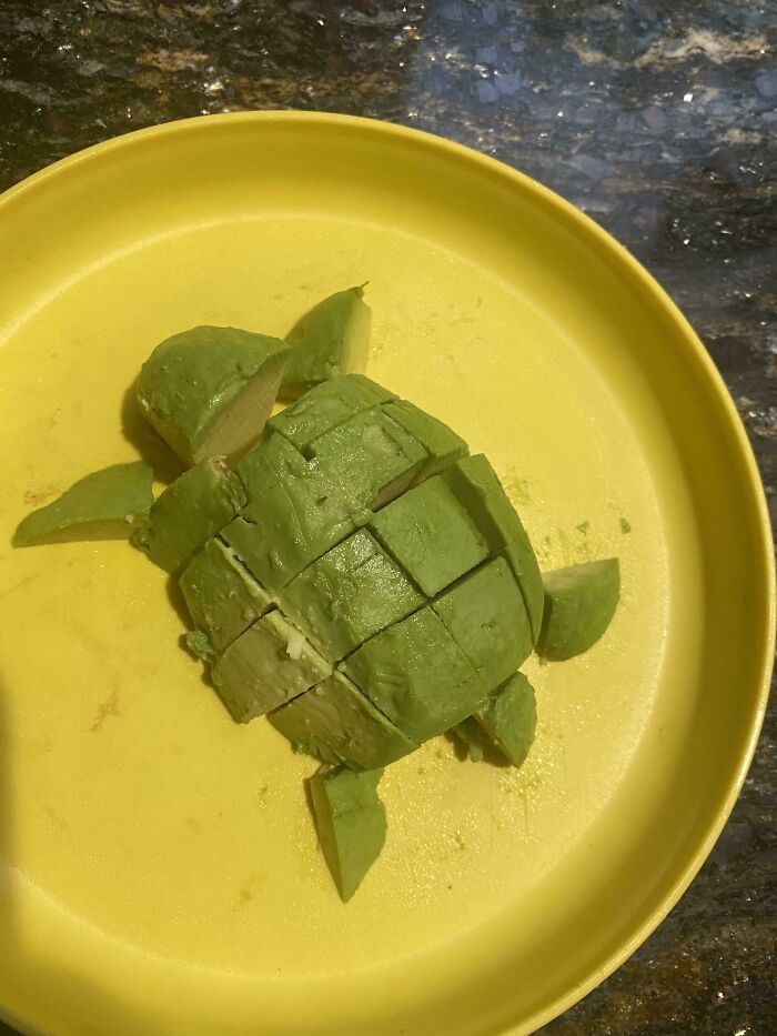 A creative arrangement of cut avocado pieces forms a turtle shape on a yellow plate, an example of vegan food.