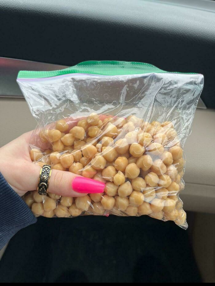 A hand holding a clear plastic bag full of chickpeas, representing unappetizing vegan food that deserves public shaming.
