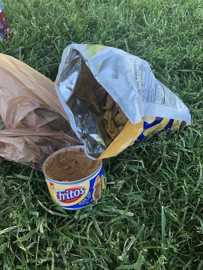 A can of Fritos bean dip next to a bag of Fritos chips on grass, showing stupid vegan food.