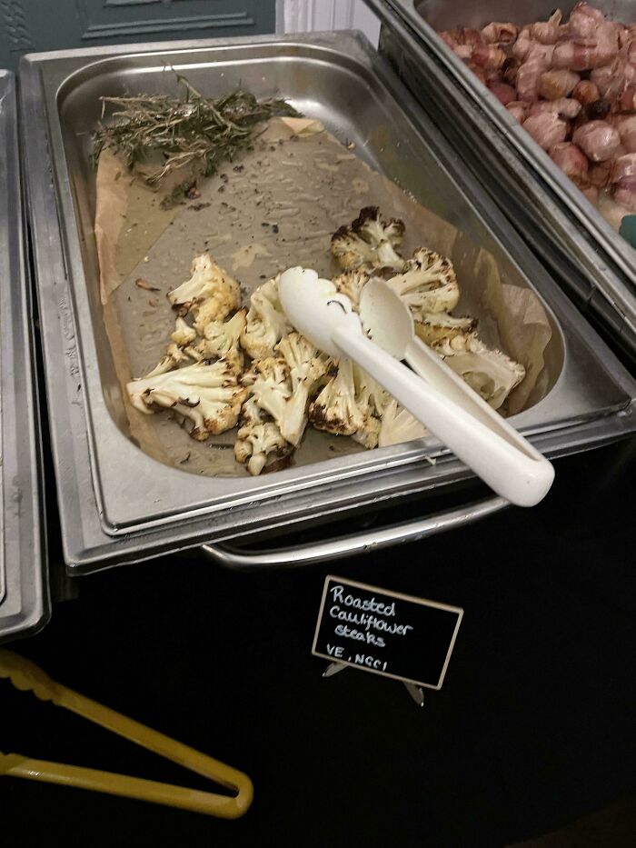 A serving tray with roasted cauliflower steaks and a sign, highlighting a piece of stupid vegan food.