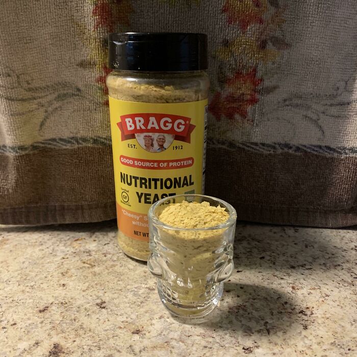 A bottle of nutritional yeast next to a skull-shaped shot glass filled with the same stupid vegan food.