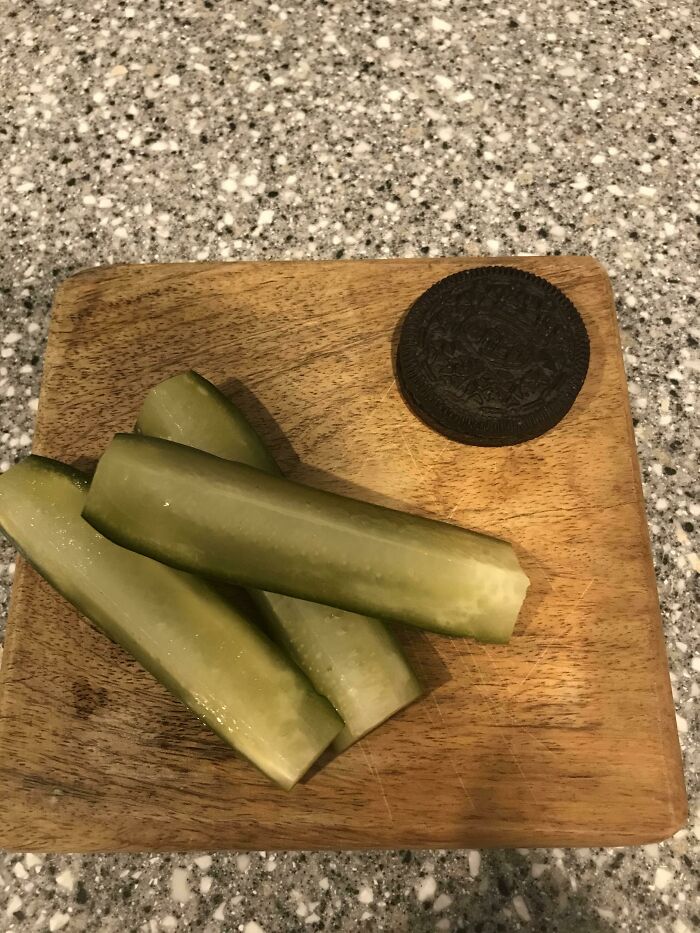 Pickle spears and an Oreo cookie on a wooden cutting board, an example of stupid vegan food.