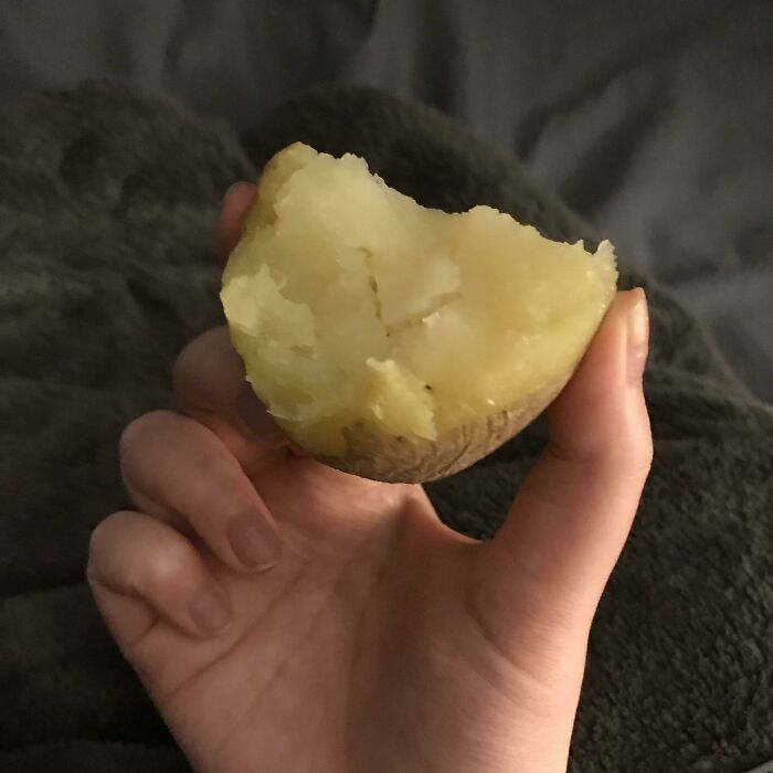 A hand holds a half-eaten boiled potato, representing another piece of stupid vegan food.