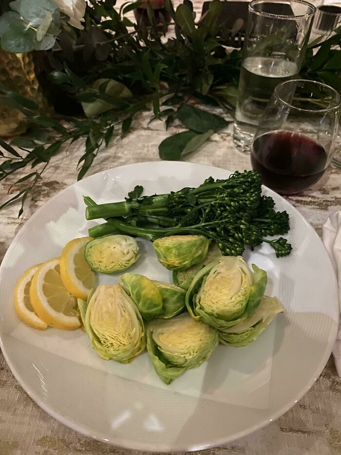 A white plate with steamed broccoli, brussels sprouts, and lemon slices, representing vegan food.