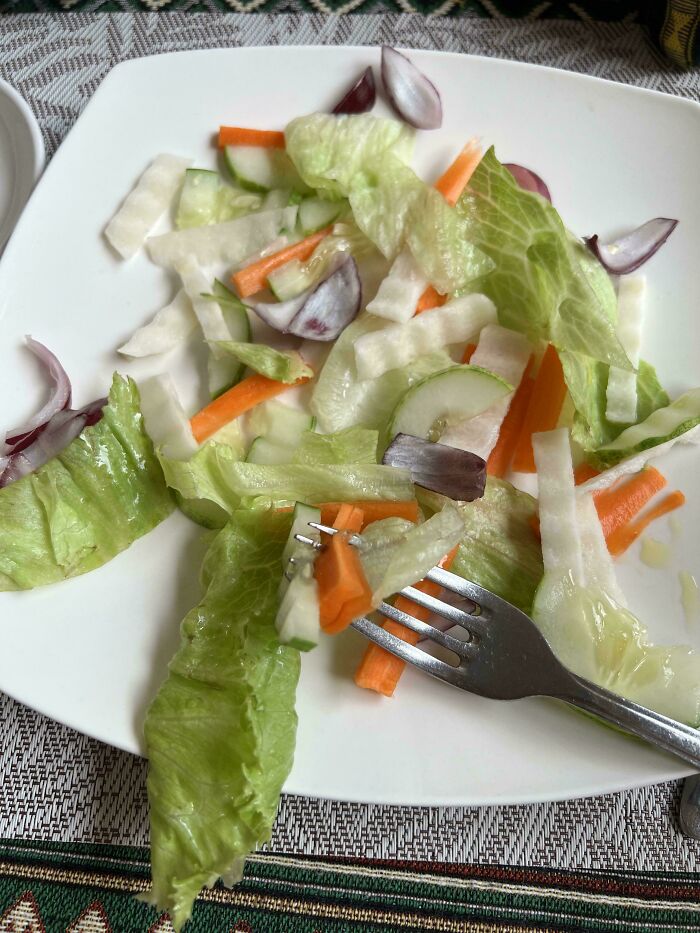 A minimalist salad of lettuce, carrots, cucumber, and red onion pieces, with a fork, a simple vegan food.