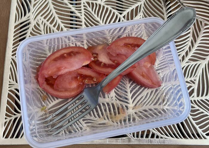Sliced tomatoes in a clear plastic container with a fork, presented as a bland vegan food option.