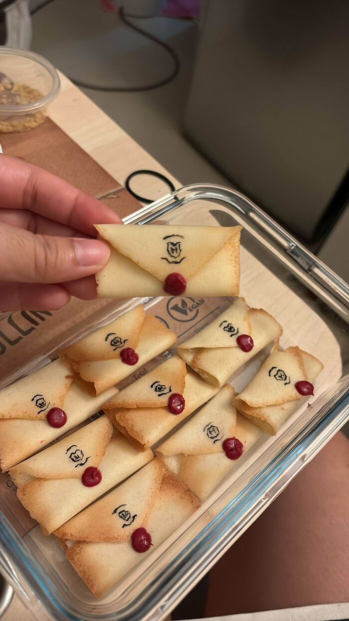 A hand holding a tiny, intricate edible envelope cookie with a wax seal, part of a collection of amazing and delicious treats by bakers.