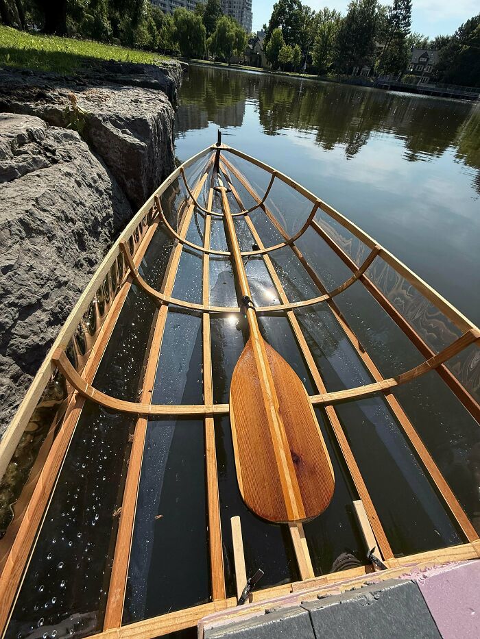 A transparent canoe with wooden frame and a wooden paddle on a calm lake, showcasing creative home DIY projects.