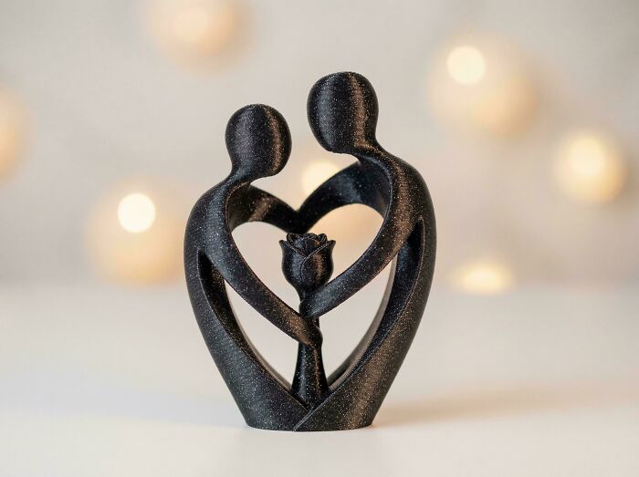 A black sparkly 3D printed figurine of two abstract figures forming a heart around a rose, a useful print.