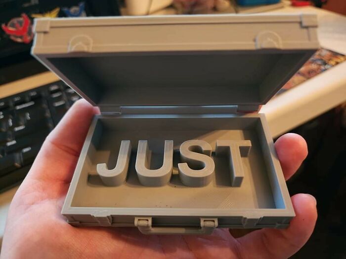 A hand holding a small 3D printed briefcase with the word JUST inside, a cool print.
