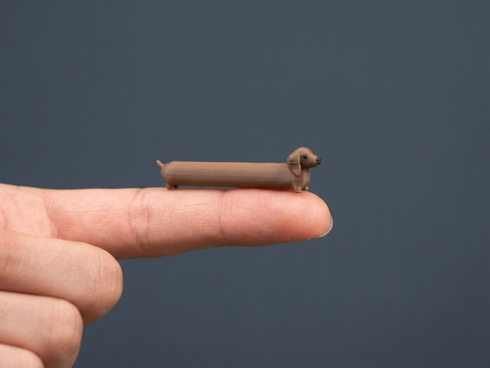 A tiny, long dachshund figurine balanced on a finger, among the cool and useful things people printed with their 3D printers.