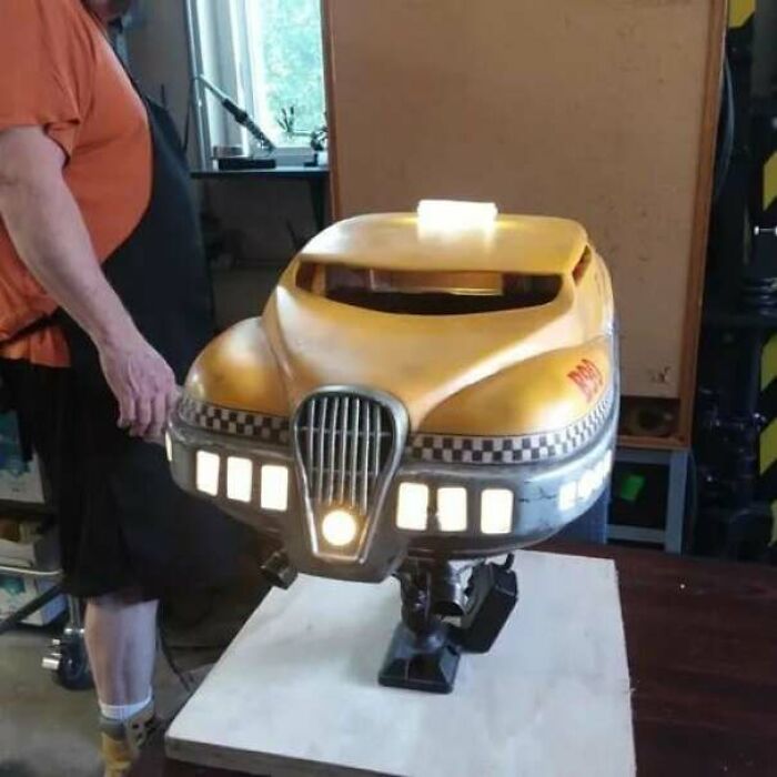 A person holding a yellow 3D printed taxi model with illuminated lights on a wooden table.