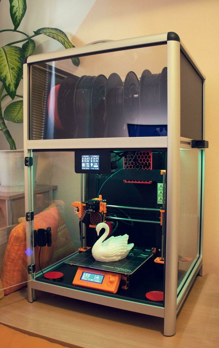 A 3D printer in an enclosure, actively printing a white swan, demonstrating useful things people printed.