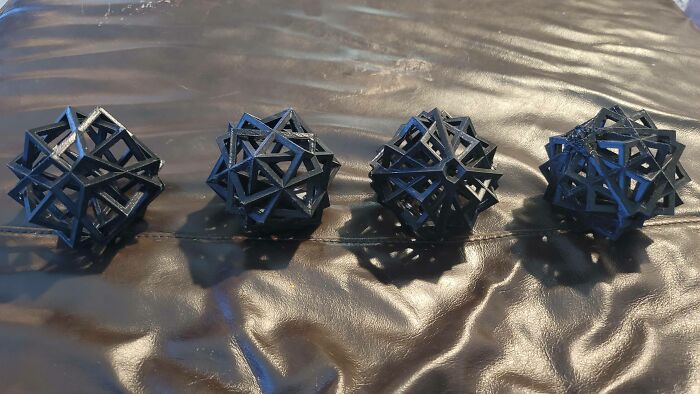 Four black geometric 3D printed objects with intricate designs, demonstrating cool things people printed with 3D printers.