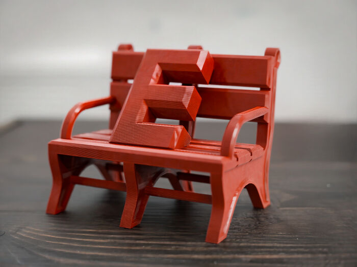 A red 3D printed miniature bench with a large red letter E on it, showcasing cool and useful 3D prints.