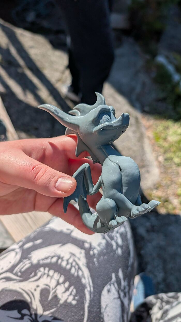 A hand holding a small, gray 3D printed dragon figure, a cool and useful thing people printed with their 3D printers.