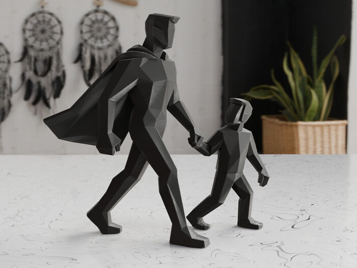 A black, low-polygon 3D printed figurine of a man with a cape walking with a child, highlighting useful things people printed with their 3D printers.