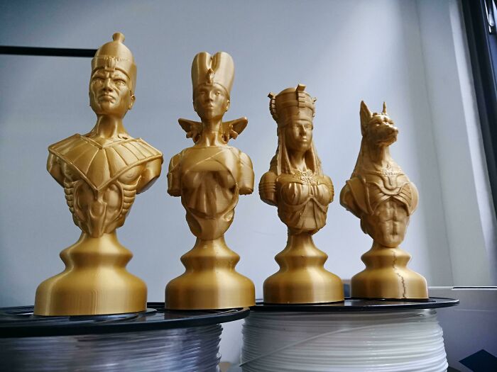 Four golden 3D printed busts of ancient Egyptian figures, including a pharaoh and an animal-headed deity.