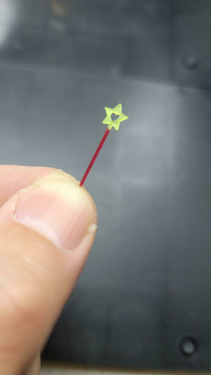 A person holding a tiny 3D printed yellow star with a heart cutout on a thin red stick.
