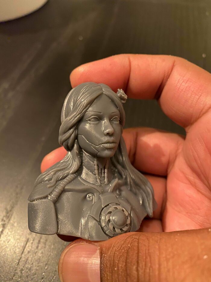 A hand holding a gray 3D printed bust of a woman with a futuristic, cybernetic design.