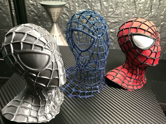 Three Spider-Man busts, one gray, one blue skeletal, and one red and black, all printed with a 3D printer.