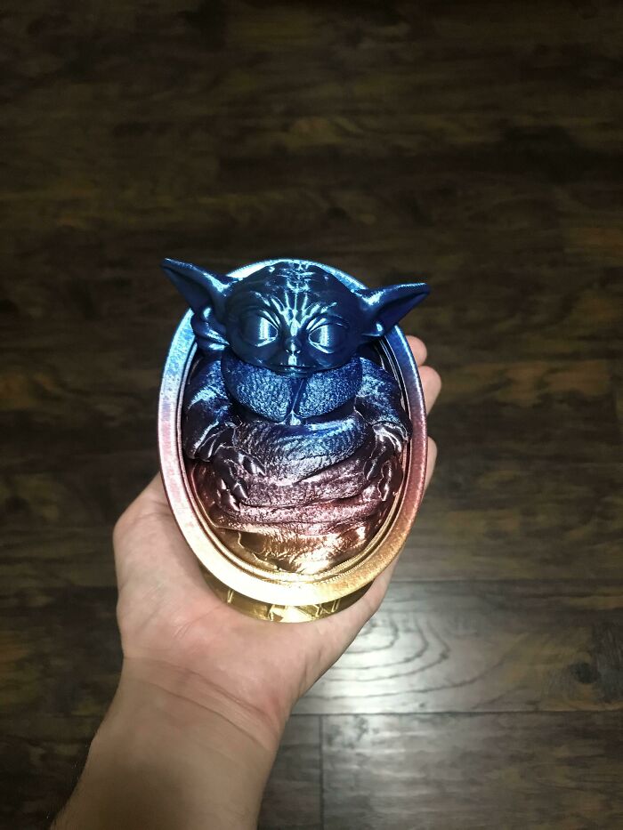 A hand holding a vibrant, iridescent 3D printed Baby Yoda figure, showcasing cool and useful things people printed.