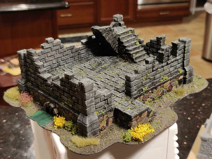 A miniature 3D printed stone ruin with moss and yellow flowers, one of the useful things people printed.