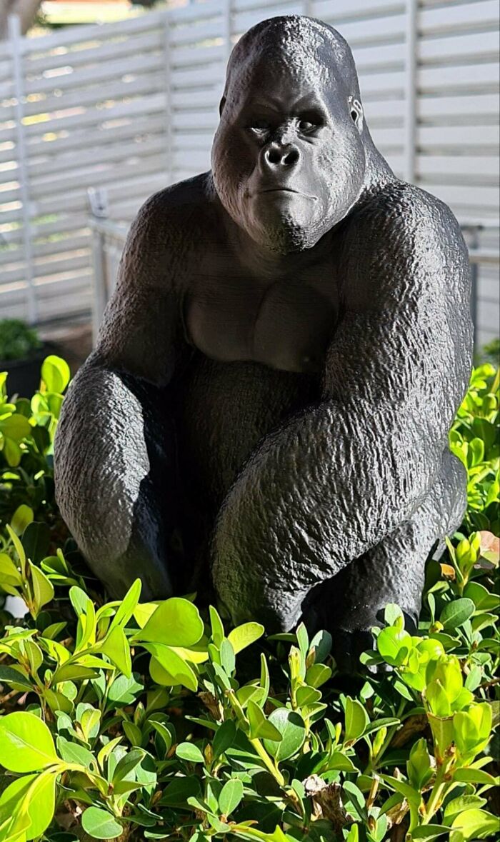 A cool 3D printed gorilla statue sits among green plants, a useful item made with 3D printers.