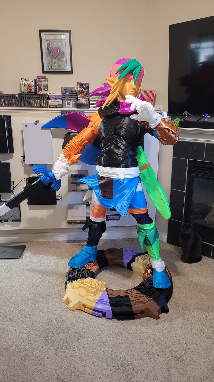 A large, colorful figure of Link from Zelda, created using a 3D printer, standing in a room with video game consoles.