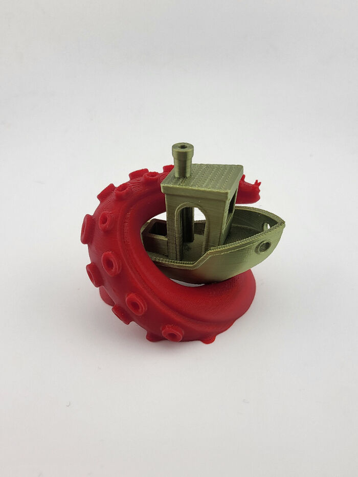 A red octopus tentacle wrapping around a small green boat, printed with a 3D printer.