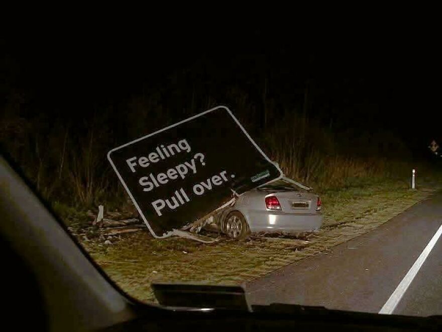 A car crashed into a road sign that says Feeling sleepy? Pull over, highlighting a rough day behind the wheel.