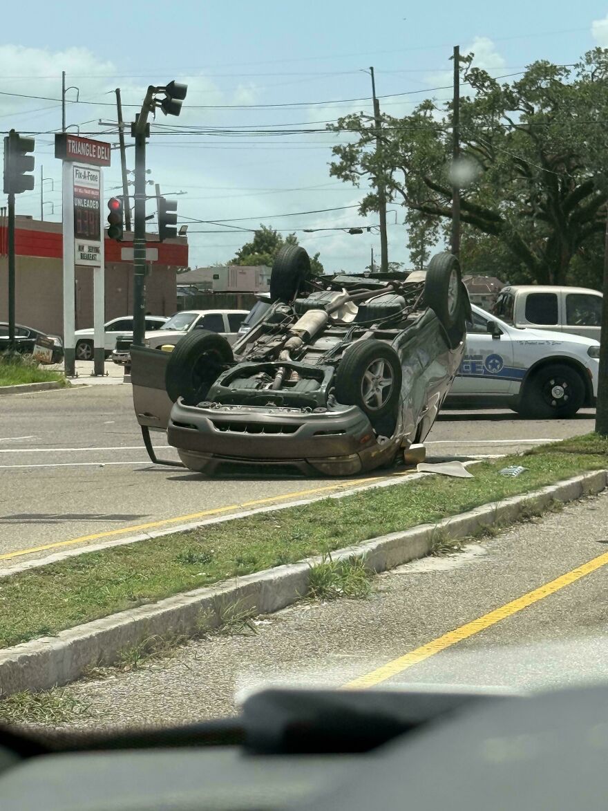 A gray SUV flipped upside down in the middle of a street intersection, showing a rough day behind the wheel.