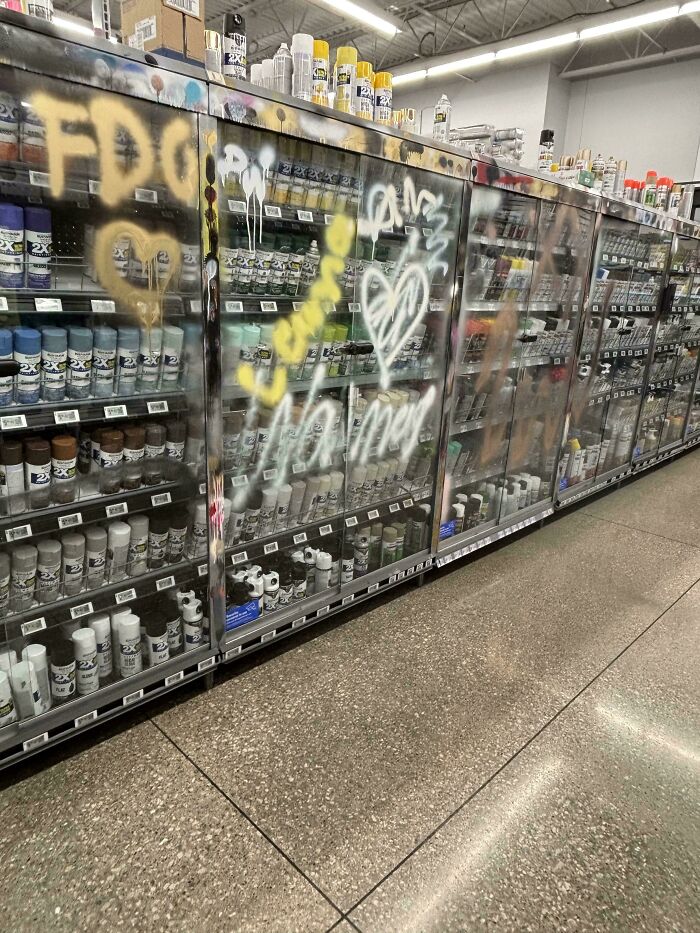 Graffiti on a display case full of spray paint cans, highlighting challenges service industry workers face.