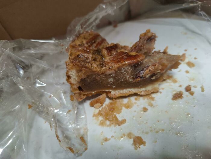 Service industry workers questioning job: a half-eaten slice of pecan pie in a plastic container, with crumbs on a white surface.