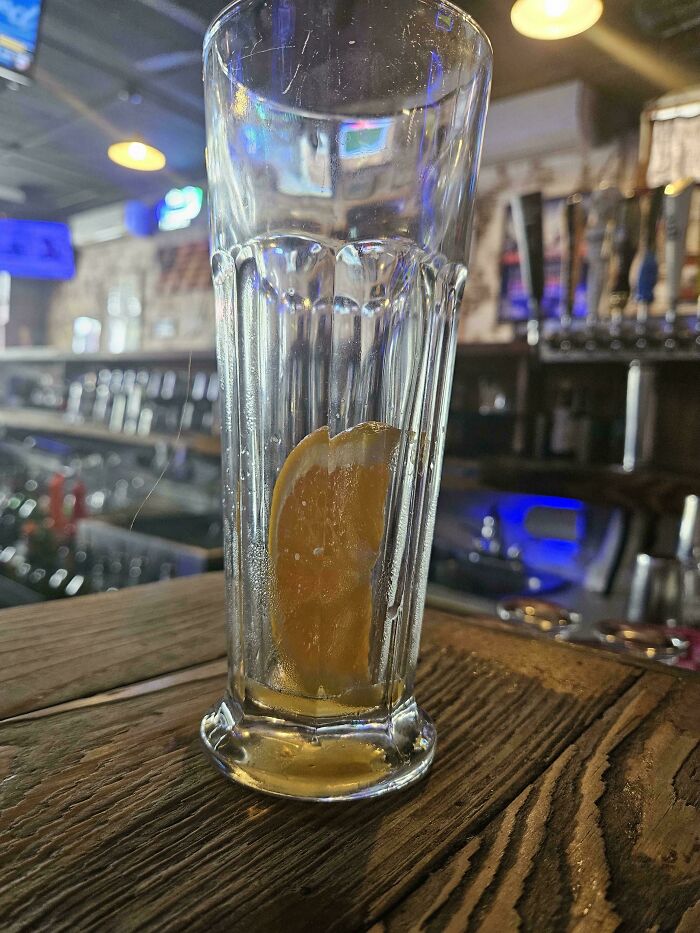 An empty glass with a lemon slice inside on a wooden bar counter, symbolizing a long day for service industry workers.