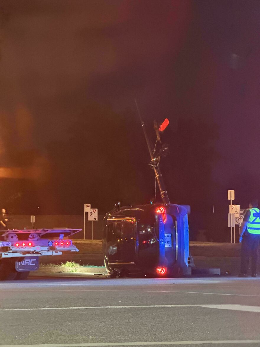 An overturned dark vehicle on a road at night with emergency lights, indicating a rough day behind the wheel.
