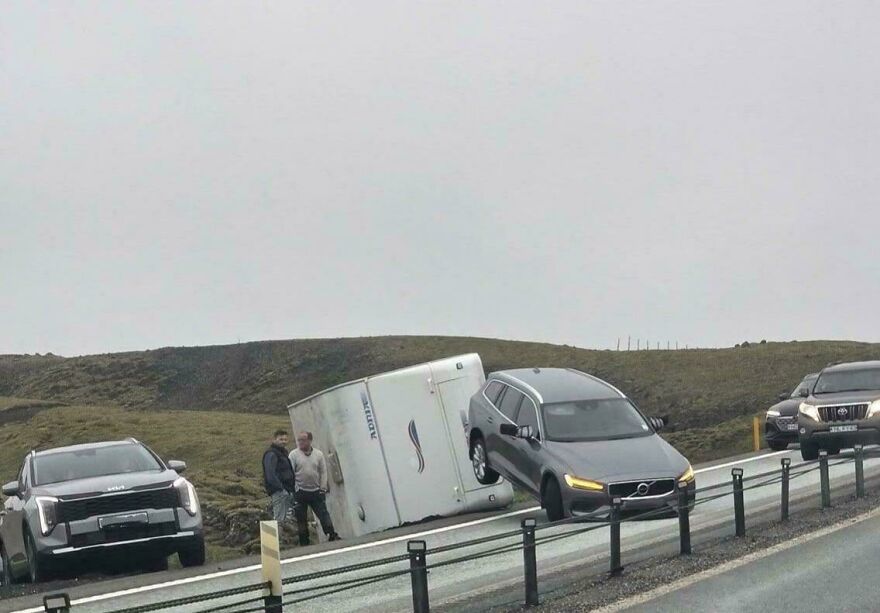 A car pulling a trailer overturned on a highway shoulder, illustrating a rough day behind the wheel.