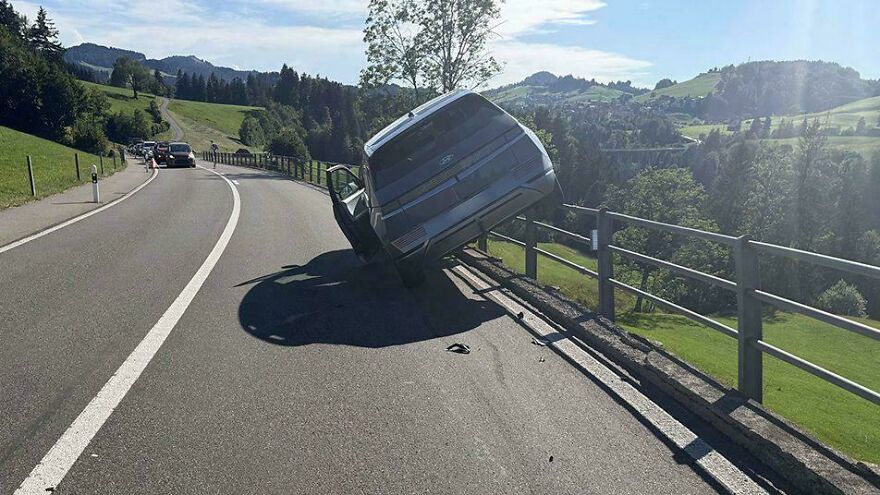 An overturned car resting against a fence on the side of a winding road, illustrating a rough day behind the wheel.