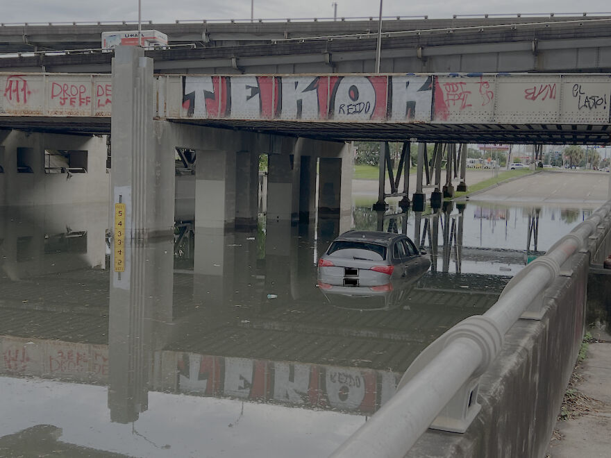 A submerged car in floodwaters under a bridge, a clear example of a rough day behind the wheel.