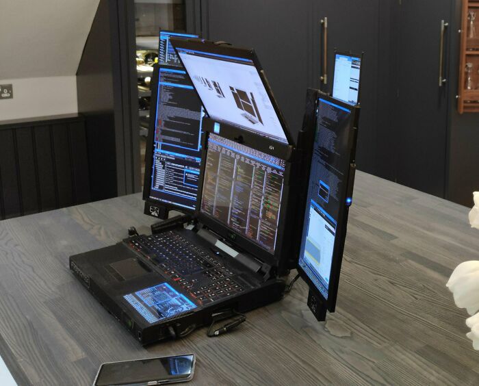 Satisfying and genius technologies: A multi-screen laptop setup on a wooden table, displaying complex code and data.