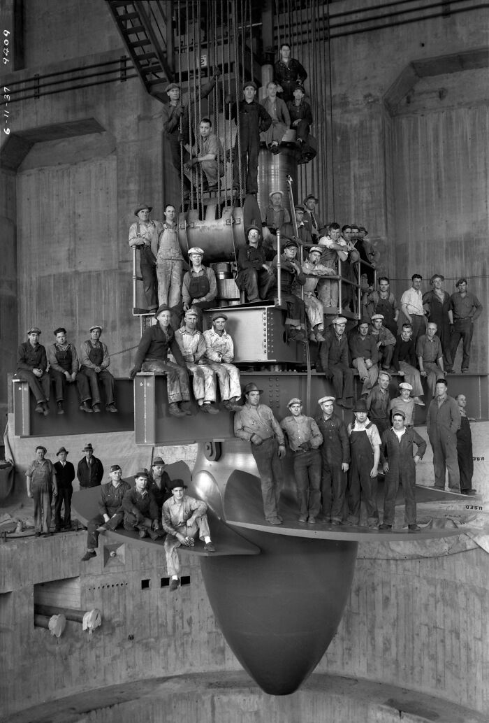 Workers posing on a massive turbine inside a dam, representing the scale of genius technologies that make everyday life easier.
