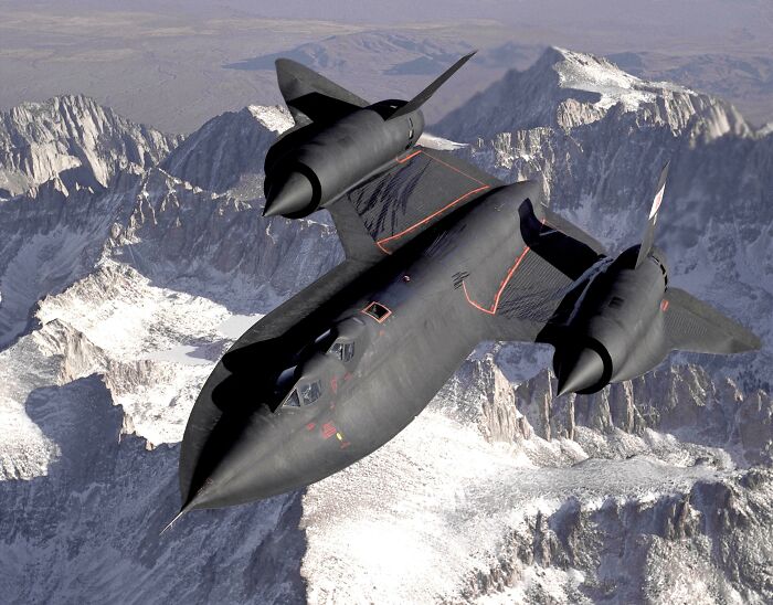 A black SR-71 Blackbird, an example of genius technologies, flies over snow-capped mountains on a clear day.