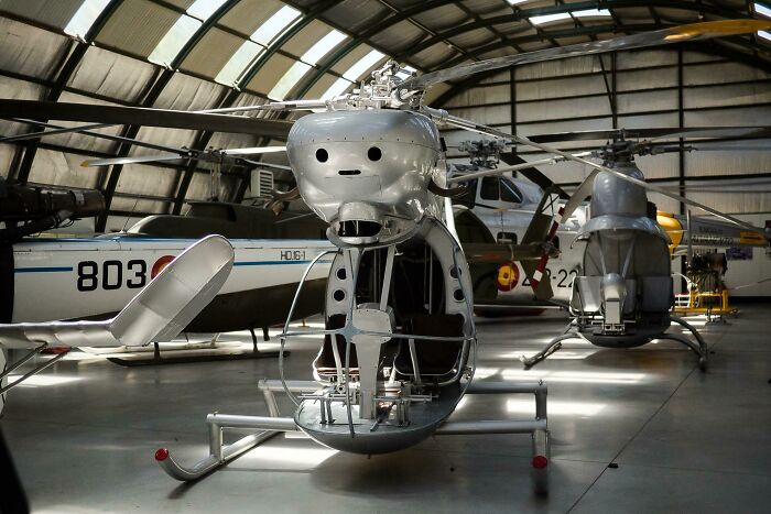 A light grey helicopter with a whimsical face on its front, parked inside a hangar, embodying genius technologies that make life easier.